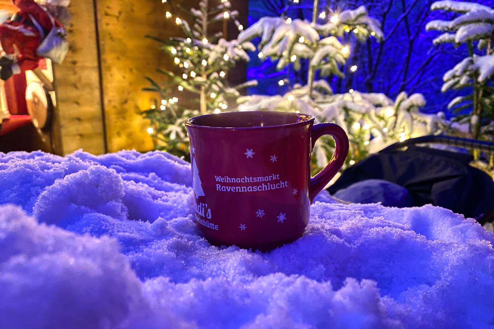 A mug of Glühwein atop snow at a German Christmas market.